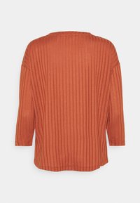 Pull en couleur rouille avec texture à côtes verticales, col rond et manches trois-quarts, offrant une coupe décontractée et un ourlet droit.