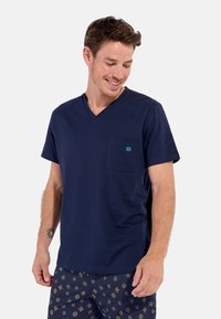 Navyblaues Baumwoll-T-Shirt mit V-Ausschnitt und kurzen Ärmeln sowie einer linken Brusttasche, die über ein kleines blaues Logo verfügt. Weicher Stoff, lässige Passform.