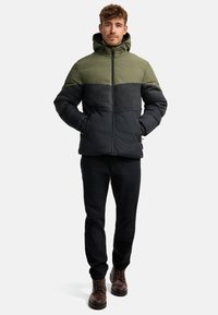 Padded jacket with a hood, featuring green, grey, and black panels. Smooth texture, zip front, and elastic cuffs. Worn with dark pants.