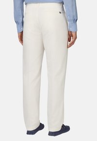 Pantaloni in lino bianchi con taglio dritto, taschino posteriore e dettagli di cucitura sottili, abbinati a scarpe slip-on blu.