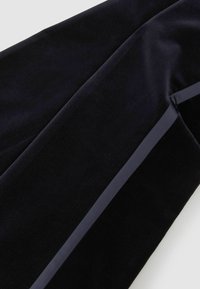 Close-up van zwart fluwelen stof met een glad satijnen lintdetail dat diagonaal over het materiaal loopt.