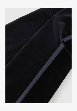 Zbliżenie czarnej aksamitnej tkaniny z gładką wstążką przypominającą satynę, biegnącą po skosie wzdłuż materiału.