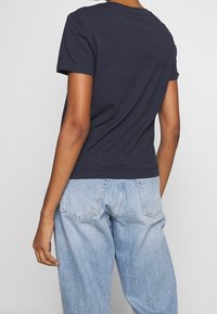 Navy blue cotton t-shirt with a rounded neckline and short sleeves, paired with light blue baggy jeans featuring back pockets and a faded texture.