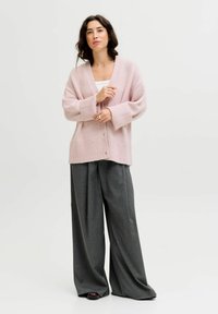 Cárdigan de punto rosa claro con escote en V y mangas largas, abrochado con botones, combinado con pantalones de pierna ancha grises oscuros.