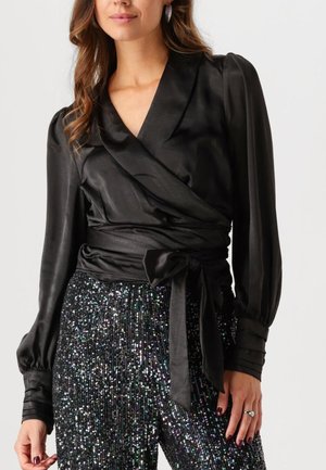 Black satin wrap top with long sleeves and a tie at the waist, paired with sequined black pants, creating a formal appearance.