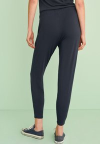 Pantalones de cintura elástica, ligeros y de color gris oscuro, con piernas cónicas. Textura suave; combinados con zapatillas de lona informales.