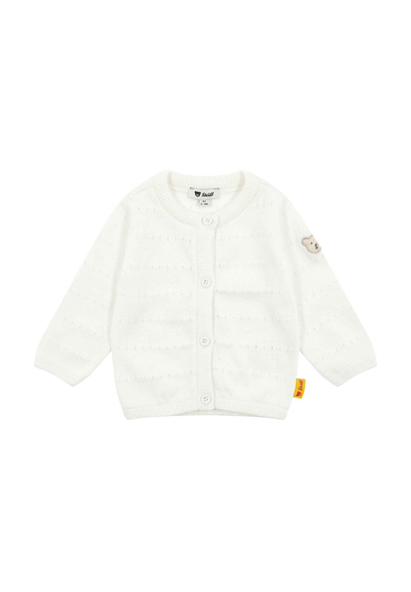 Cardigan bianco lavorato a maglia con maniche lunghe, cinque bottoni, motivo cucito e una toppa a forma di orso sulla manica sinistra. Presenta un'etichetta gialla.