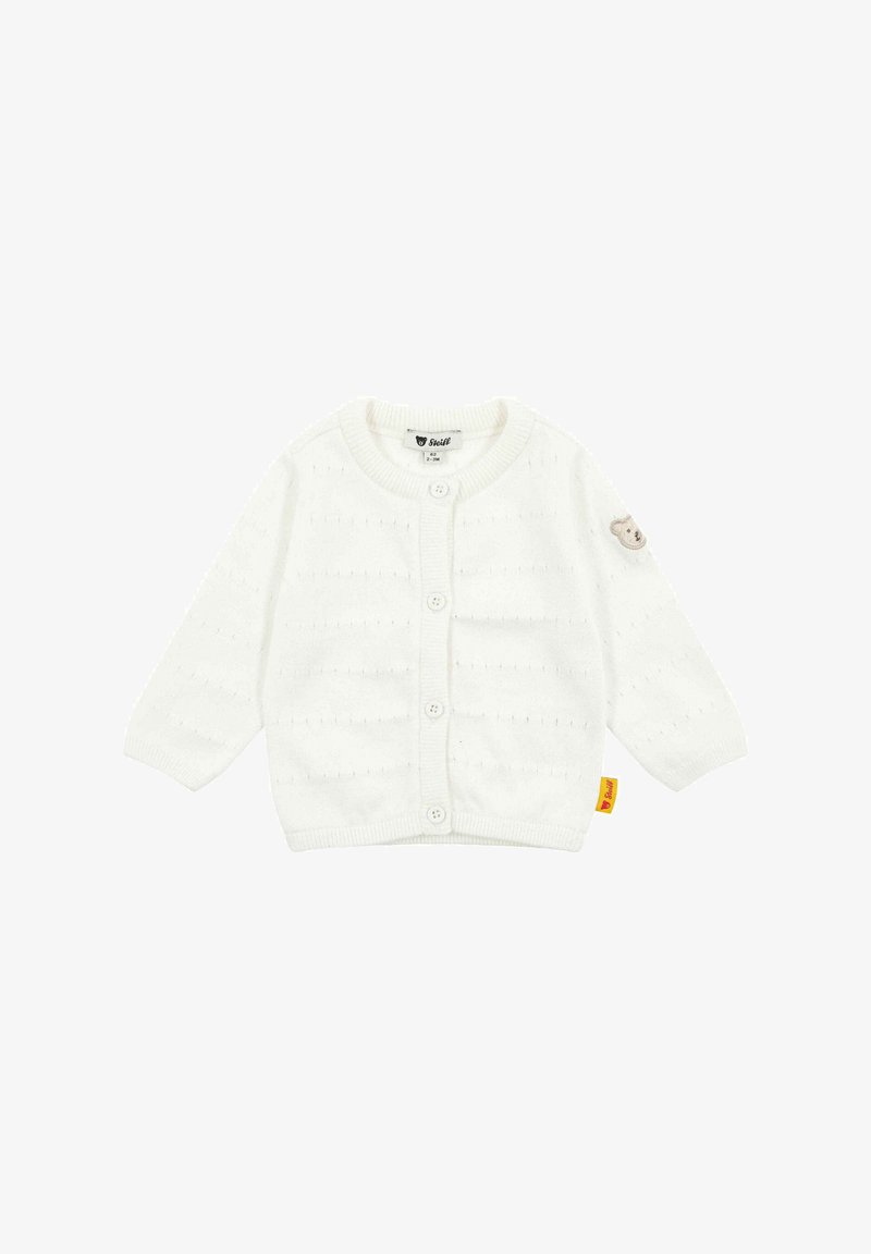 Cardigan bianco lavorato a maglia con maniche lunghe, cinque bottoni, motivo cucito e una toppa a forma di orso sulla manica sinistra. Presenta un'etichetta gialla.