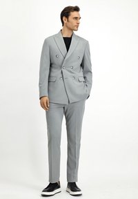 Szary, dwurzędowy garnitur z teksturowanej tkaniny, o slim fit, z klapami w kształcie notcha, w połączeniu z gładkimi czarnymi butami typu slip-on.