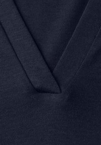 Nærbillede af marineblå V-hals sweaterstof, der viser strikkestruktur og detaljer med ribbet halsudskæring.