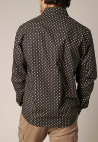 Zwarte shirt met kleine gouden schedelpatronen, lange mouwen, een kraag en een rechte zoom. Textielstof met een gladde afwerking.