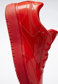 Błyszczący czerwony sneaker Reebok z grubą podeszwą, przeszyciami, sznurówkami i logo z boku na białym tle.