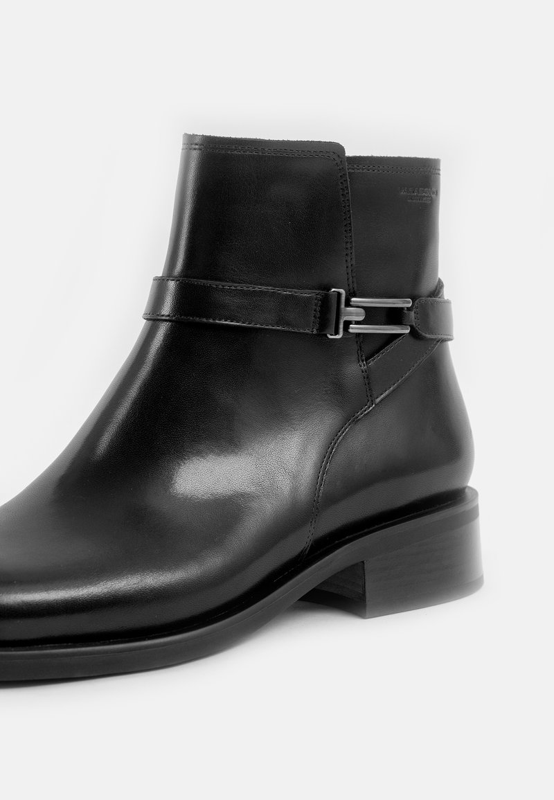 Czarny skórzany botek za kostkę o błyszczącym wykończeniu, z bocznym paskiem i srebrnym detalem w postaci klamry, oraz niskim, klejonym obcasem.