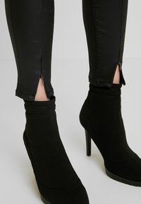 Leggings negros ajustados con puños con cremallera, combinados con botines de tacón alto negros. El material parece suave, con textura mínima.