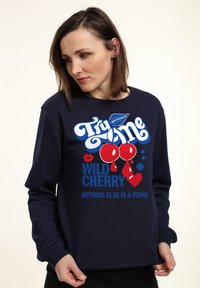 Granatowy sweatshirt z dużą grafiką przedstawiającą czerwone wiśnie, niebieskim napisem "Spróbuj Mnie Dzika Wiśnia" oraz kontrastowymi elementami wzorniczymi.