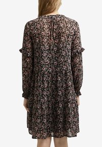 Vestido floral con fondo negro, adornado con flores rosas y verdes. Mangas largas con puños rizados y una silueta fluida.