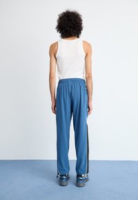 Blue athletic pants with an elastic waistband, side black stripe accents, and tapering cuffs. Worn with a white tank top and sneakers.