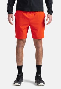 Pantaloni sportivi rossi con cintura elastica, texture liscia e lunghezza sopra il ginocchio, abbinati a scarpe sportive nere e calze.