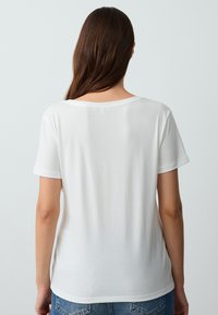 T-shirt bianco a maniche corte in un tessuto morbido e leggero, caratterizzato da un collo rotondo e una vestibilità rilassata, mostrato da dietro.