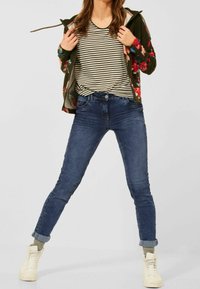 Grön jacka med blommönster, randig topp, blå skinny jeans, vita högskor. Har uppvikta ärmar och avslappnad passform.