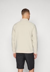 Light beige jacket with a stand-up collar, elastic cuffs, and hem. The material appears smooth, paired with black shorts.