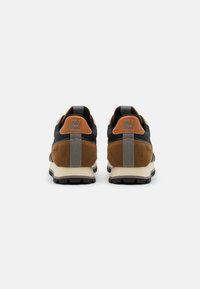 Sneaker marroni e neri realizzati in materiali scamosciati e tessili. Caratteristiche includono un tassello sul tallone grigio, dettagli in tan e suola in gomma testurizzata.