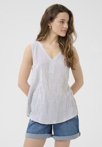 Blouse sans manches rayée en blanc et bleu, présentant un décolleté en V et une coupe décontractée. Portée avec un short en denim à ourlet retroussé. Texture de tissu lisse.
