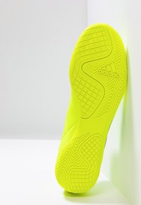 Suola di scarpa sportiva gialla brillante con un motivo di presa strutturato; presenta un marchio prominente e un design curvo distintivo, mostrata su uno sfondo neutro.