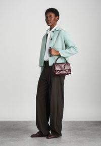 Ανοιχτό μπλε παλτό από μάλλινο ύφασμα, λευκό πουκάμισο, καφέ παντελόνι φαρδιάς γραμμής και μια μικρή μπορντό τσάντα με επένδυση και ασημένιο κούμπωμα. Λείες υφές.