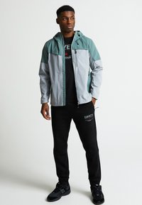 Meeste kergehall ja türkiissinine jakk, millel on lukuga esiosa, reguleeritav kapuuts ja must logo T-särk. Kombineeritud mustade spordipükste ja tossudega.