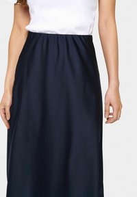 Jupe en satin bleu marine avec une taille élastique, texture lisse et longueur complète, associée à un t-shirt blanc.