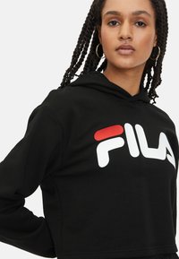 Sudadera corta negra hecha de tela suave, con un logo blanco y acentos rojos. Diseño con capucha y un ajuste relajado, con puños acanalados.