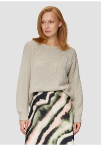 Beige gestrickter Pullover mit Perlenakzenten in einem spiralförmigen Muster; kombiniert mit einem mehrfarbigen Rock, der geschwungene grüne und rosa Designs zeigt.