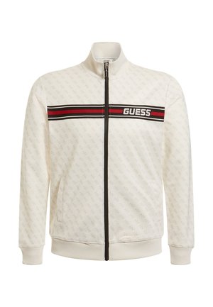 Chaqueta blanca con cremallera y cuello alto, patrón sutil, banda a rayas roja y negra con el logo "GUESS" en el pecho. Puños y dobladillo acanalados.