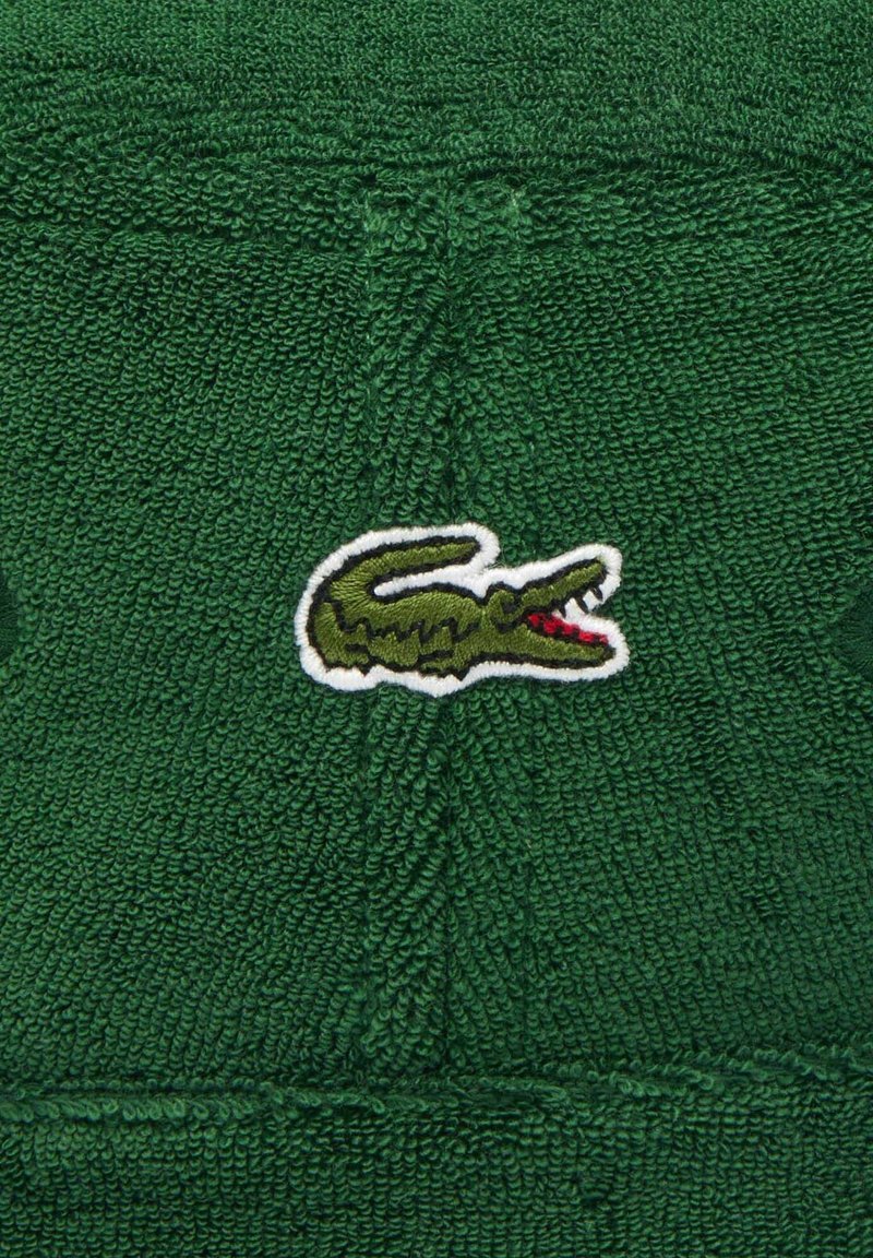 Zielony ręcznik z materiału frotte z haftowanym logo krokodyla w zielonym i czerwonym kolorze, o fakturowanej powierzchni i jednolitym kolorze.