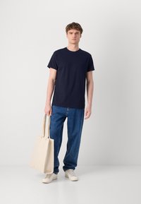 Mørkeblå bomulls t-skjorte, avslappet passform, rund hals; sammen med lyseblå jeans med rette ben, holder en beige canvas tote bag.