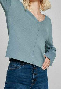 Maglione corto azzurro chiaro con scollatura a V, texture a coste e maniche lunghe, abbinato a jeans in denim blu a vita alta con chiusura a bottoni.