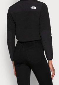 Chaqueta de felpa recortada negra con mangas de nailon negro, logo en la parte superior de la espalda, cuerpo texturizado y acentos de tela suave en las mangas.