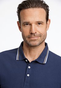 Mörkblå polo med tre knappar, med en ribbad krage i vitt och beige. Slät bomullsmaterial. Närbild på halslinningen.