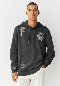 Donkergrijze hoodie van een katoenmix. Heeft bloemen- en vlinderborduursels, een voorzak en een verstelbare trekkoordcapuchon.