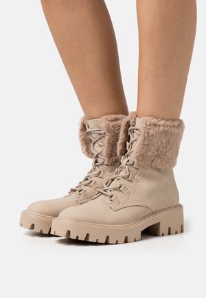 Bottes beiges à lacets avec une semelle épaisse et un revers en fausse fourrure, en cuir lisse avec des oeillets renforcés pour les lacets.