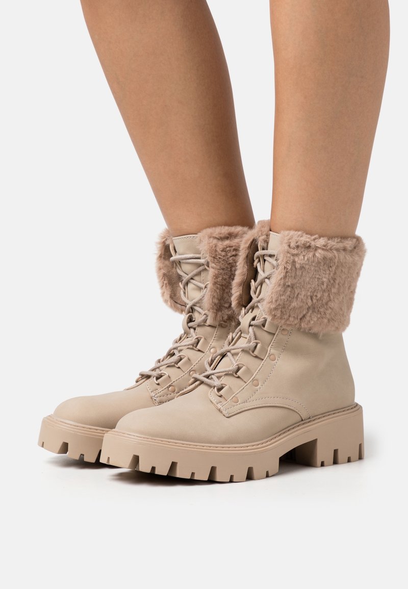 Bottes beiges à lacets avec une semelle épaisse et un revers en fausse fourrure, en cuir lisse avec des oeillets renforcés pour les lacets.