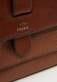 Brązowa skórzana torba o teksturowanej powierzchni z dopasowanym skórzanym paskiem i złotym logo Fossil.