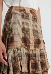 Falda marrón con estampado y dobladillo con volantes, que presenta una tela ligera y texturizada, y una cintura ajustada que se transforma en un diseño fluido.
