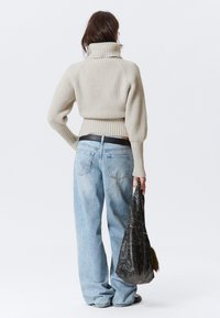 Cremfarbener gerippter Rollkragenpullover, hoher Kragen, oversized Schnitt, kombiniert mit hellblauen, locker sitzenden Jeans und einer schwarzen strukturierten Umhängetasche.