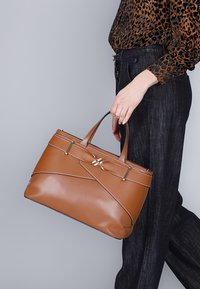 Borsa a mano in pelle marrone con design strutturato, dotata di due manici superiori, dettagli in metallo argentato e cuciture diagonali.