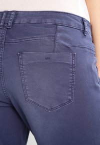 Close-up van een persoon die indigo blauwe denim jeans draagt, met zicht op de achterzak en de riemlussen.