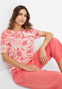 Koralle-farbenes Kurzarmoberteil mit weißen Blumenmuster, runder Ausschnitt, kombiniert mit passenden koralle-farbenen Hosen. Glattes Baumwollgemisch.