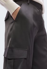 Tmavomodré cargo nohavice s matným saténovým povrchom, s bočným vreckom, rovný predný diel a príťažlivý strih. Tkanina má hladkú textúru a jemný lesk.