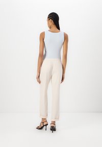 Top senza maniche di un blu chiaro con scollatura rotonda, abbinato a pantaloni larghi color crema arrotolati e sandali neri con cinturini.